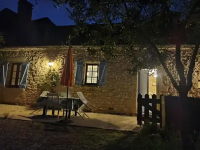 Façade en pierre du gîte Les Figuiers illuminée le soir avec terrasse